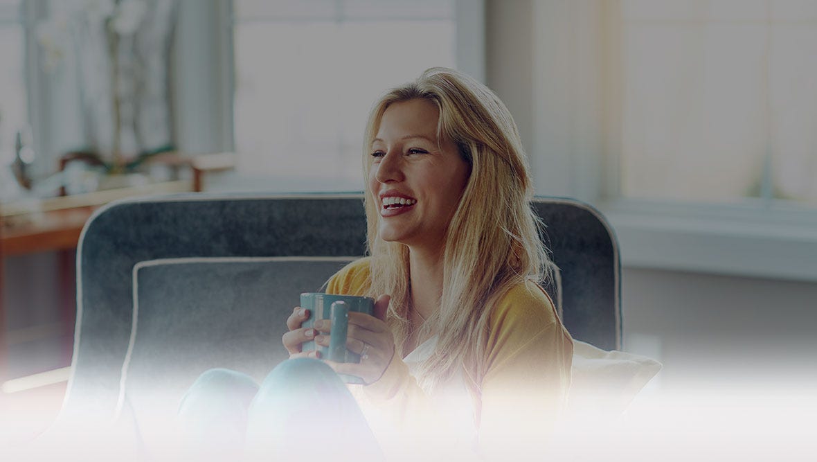 Smiling women, sitting in an oversized chair, holding a coffee cup.